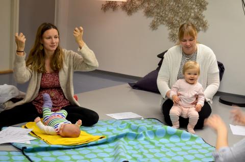 Vauvaviittomakurssilla kaksi naista istuu lattialla. Toisella on vauva sylissä, toisella maassa edessä.