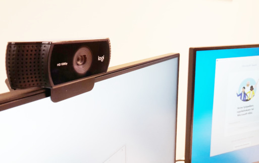 Kaksi tietokoneen näyttöä, toisessa ylälaidassa kiinni pieni videokamera.